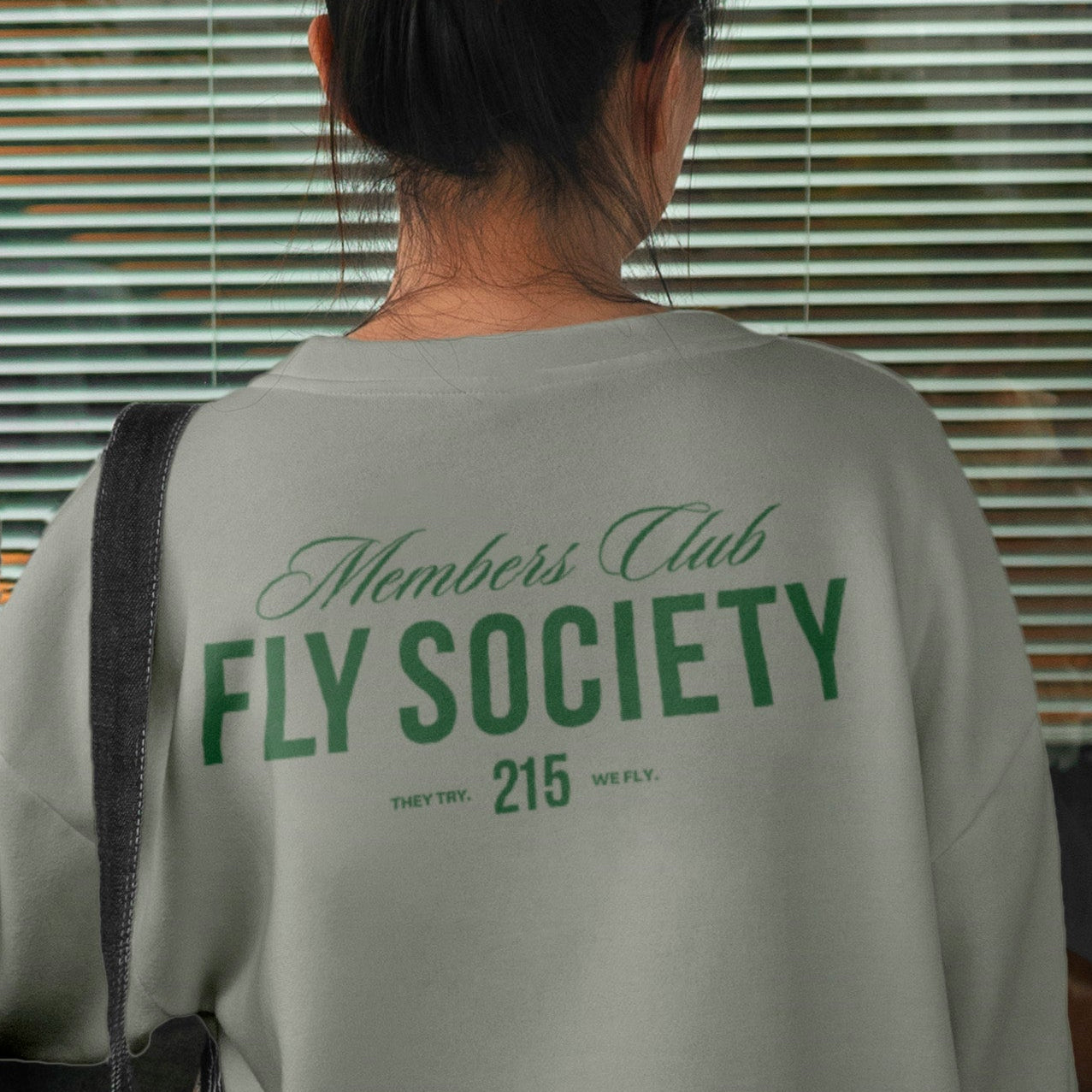 Person wearing a light gray sweatshirt with 'Fly Society' text, standing indoors.