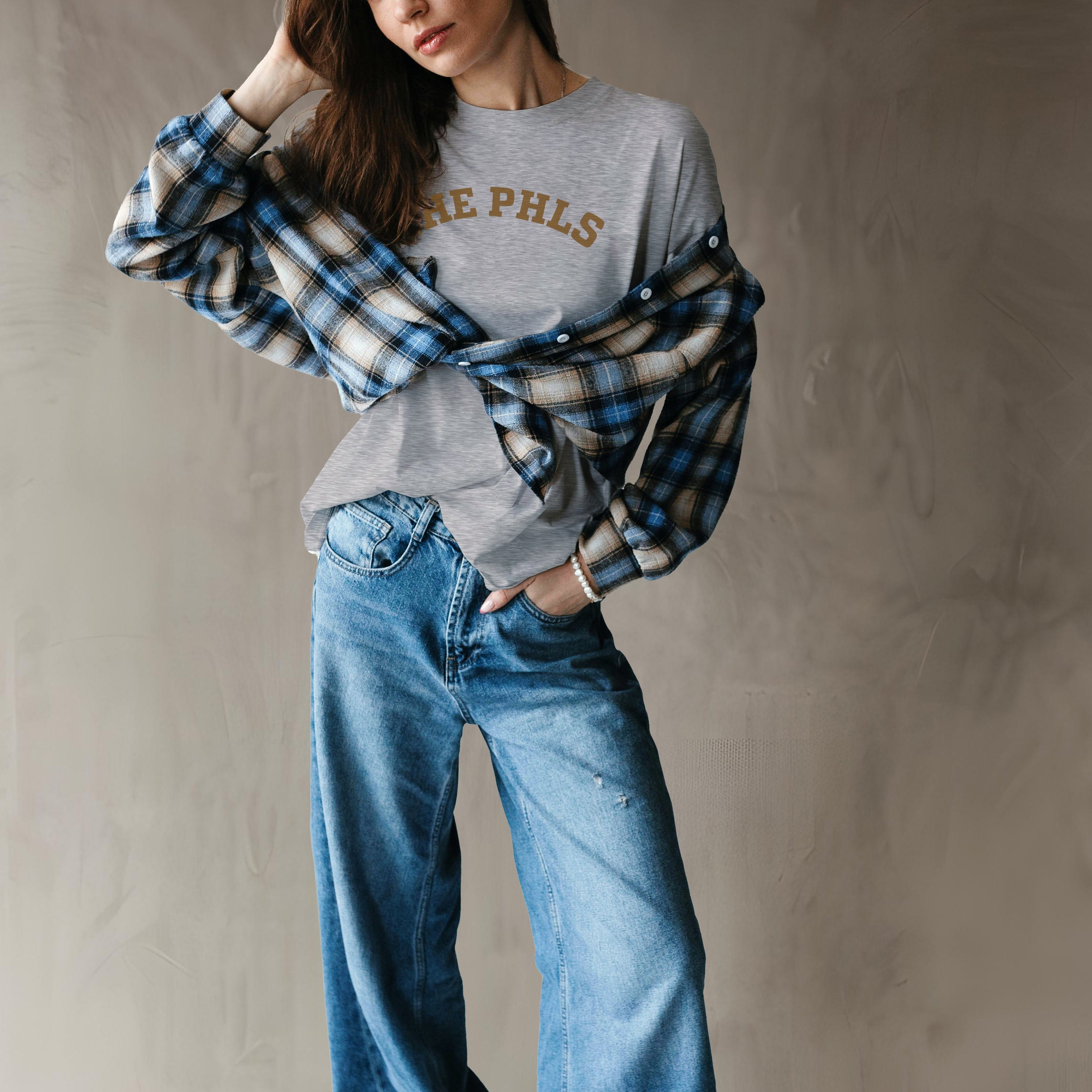 Person wearing a gray sweatshirt with 'PHILS' text, plaid shirt, and blue jeans against a plain background