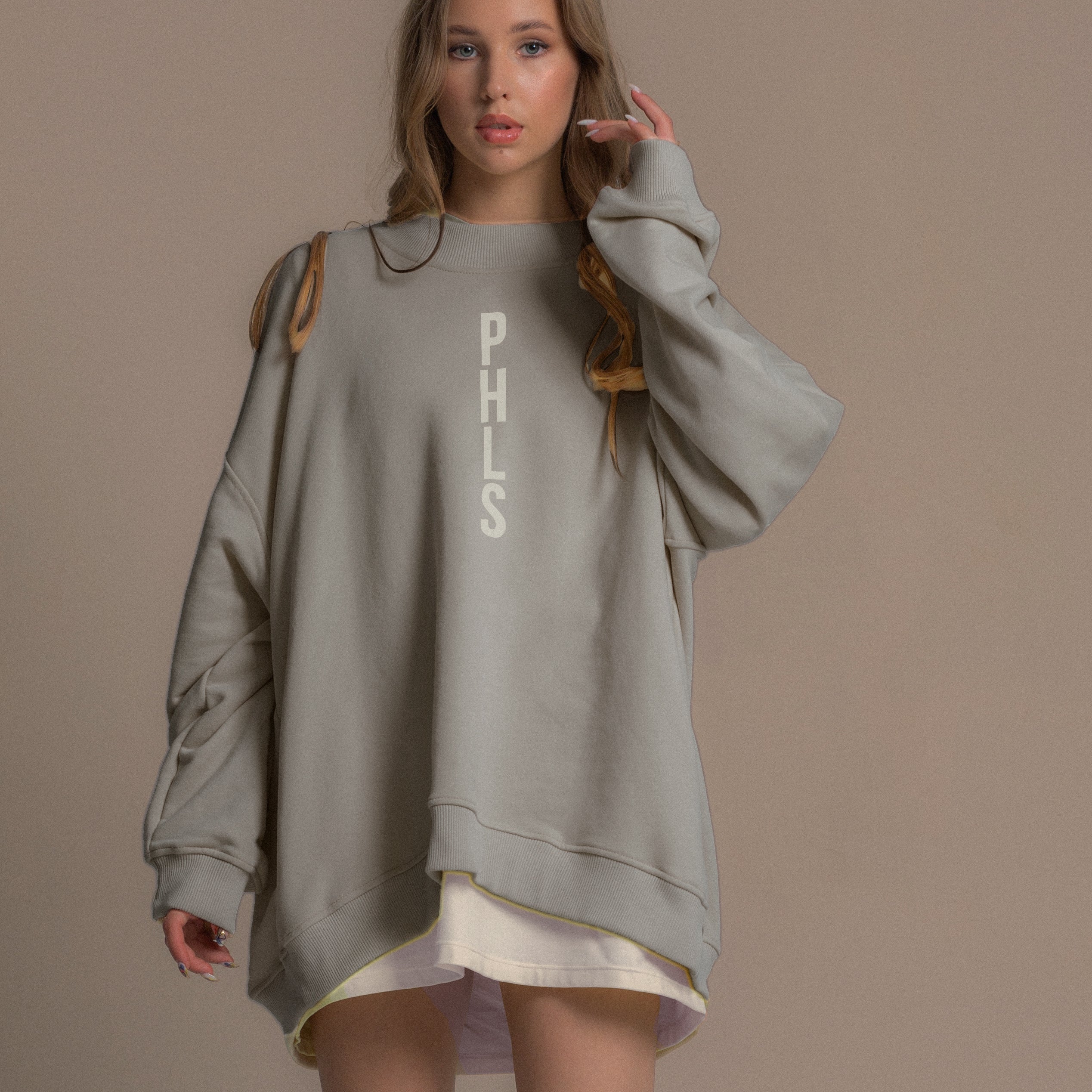 Woman wearing a gray oversized sweatshirt with 'PHLS' text on a beige background