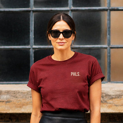 Woman wearing a burgundy t-shirt and black leather skirt standing against a brick wall.