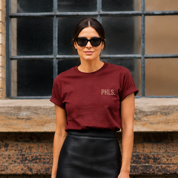 Woman wearing a burgundy t-shirt and black leather skirt standing against a brick wall.