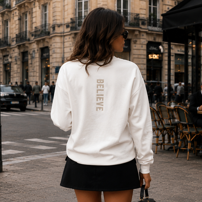 Woman walking on a city street wearing a white sweatshirt and black skirt.