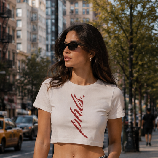 Woman walking on a city street wearing a white crop top and ripped jeans.