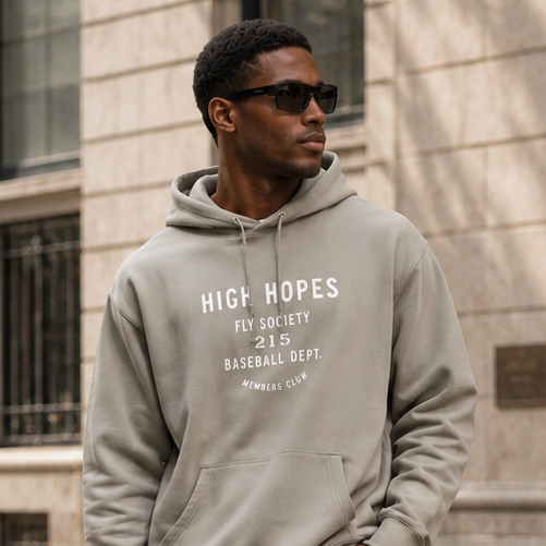Man wearing a gray hoodie with text, blue jeans, and black Adidas shoes on a city street.