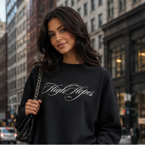Woman in black sweatshirt and light blue jeans standing on a city street.