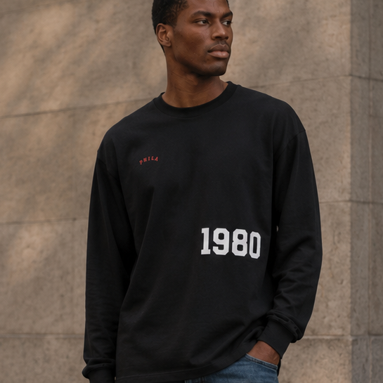 Man wearing a black sweatshirt with '1980' and blue jeans standing on a street.