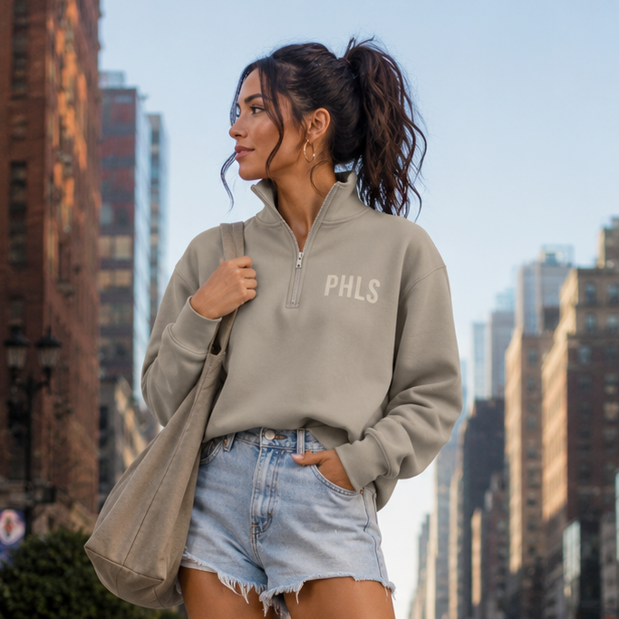 Woman in a gray sweatshirt and denim shorts standing on a city street.