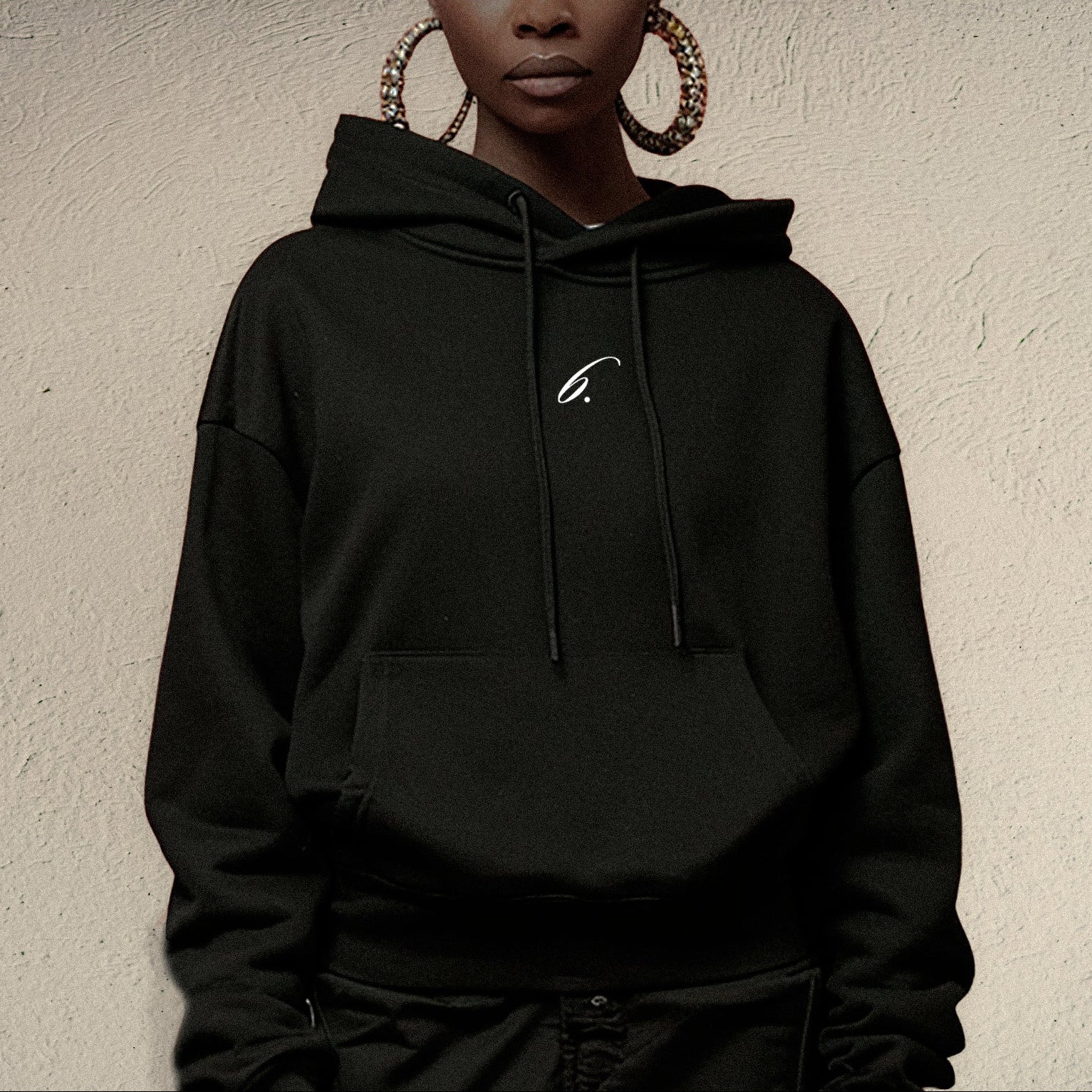 Person wearing a black hoodie with a small logo on a beige background