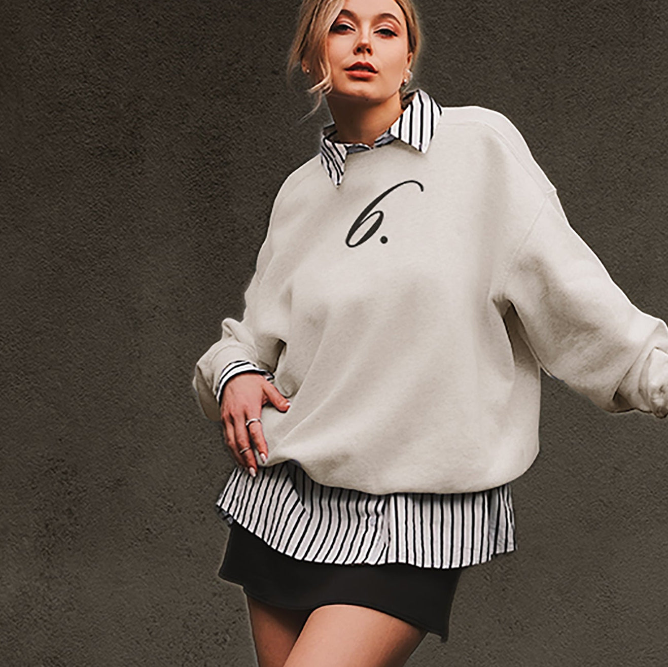 Woman wearing a white oversized sweater with a number 6 design on a dark background