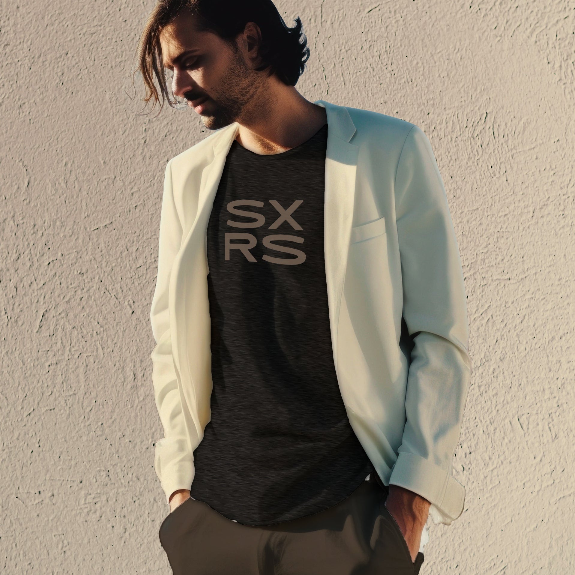 Man wearing a light blue blazer over a black t-shirt with 'SXRS' text against a plain wall.