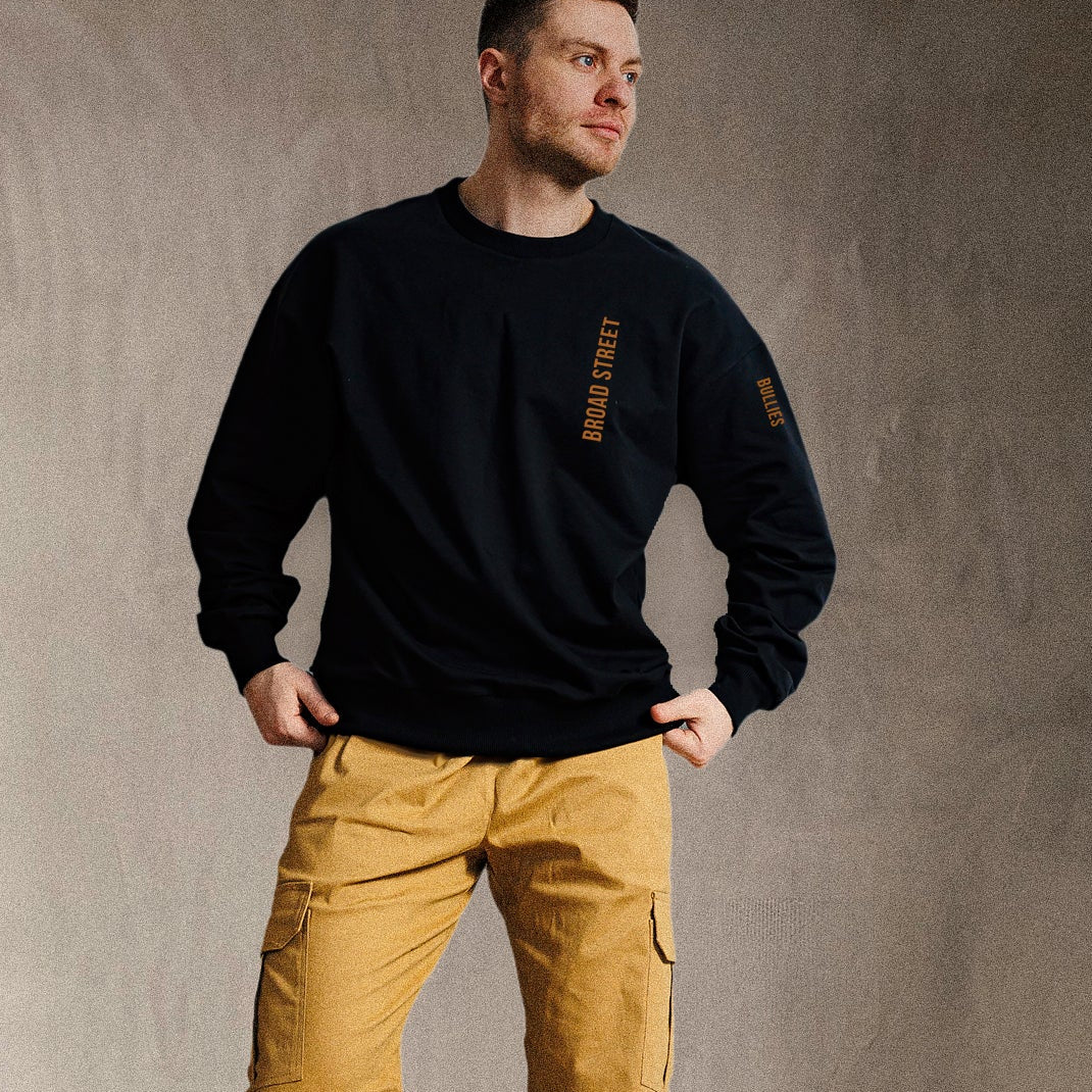 Man wearing a black sweatshirt and yellow pants against a gray background