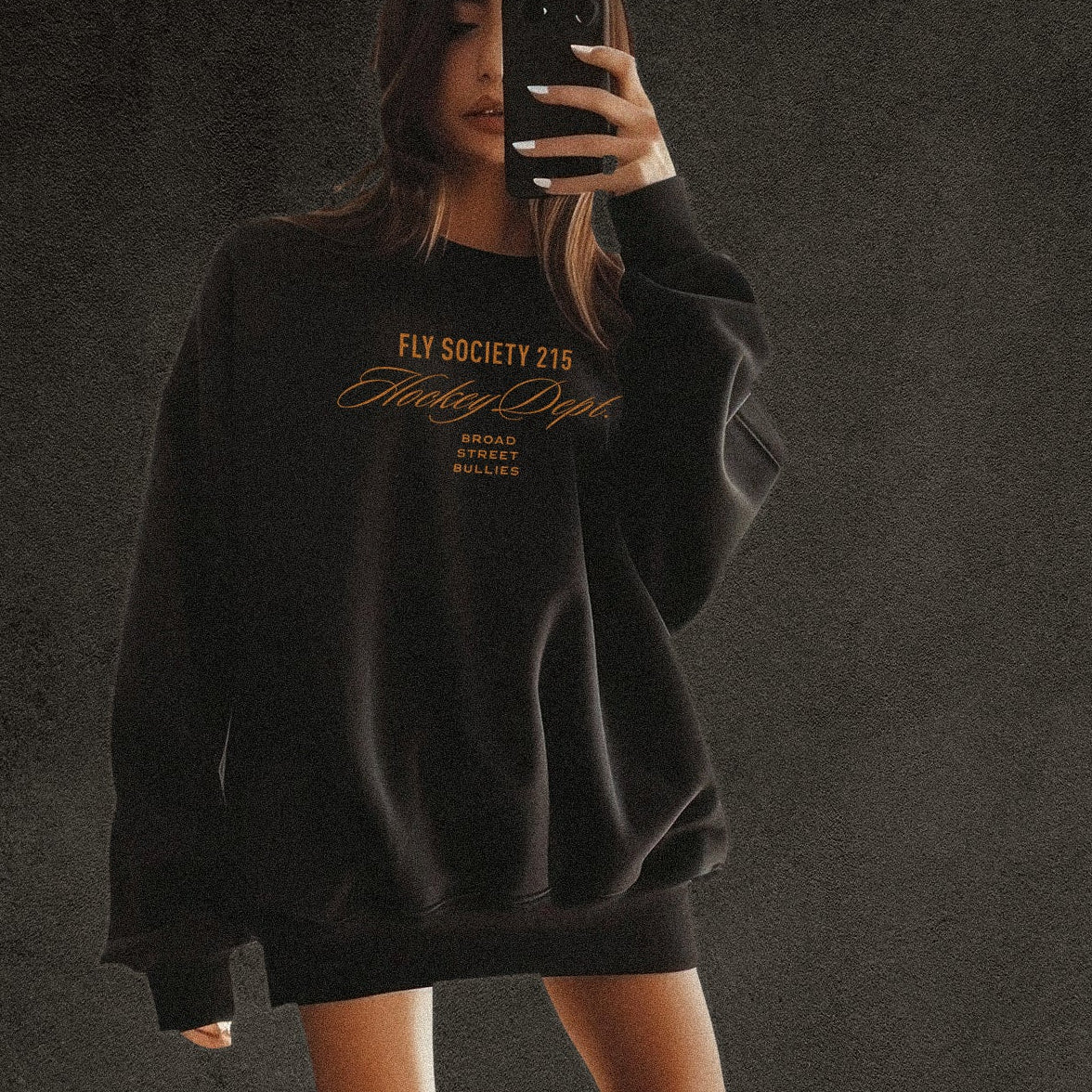 Person wearing a black sweatshirt with text, taking a mirror selfie on a dark background