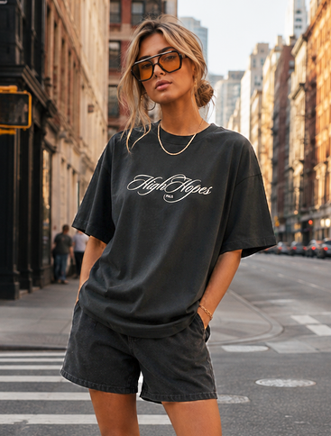 Person wearing a black t-shirt and shorts standing on a city street.