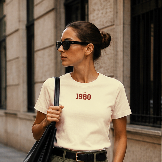 Woman walking on a city street wearing a white t-shirt with text, green cargo shorts, black loafers, and carrying a black bag.