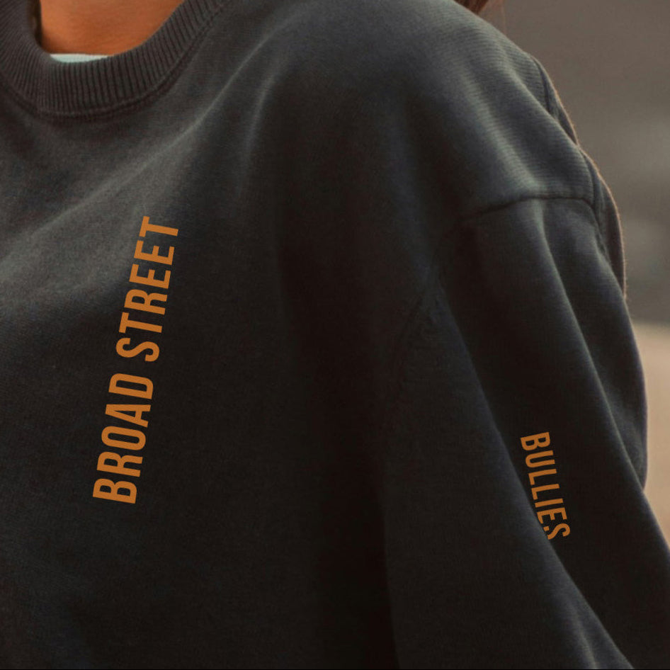 Dark sweatshirt with 'BROAD STREET BULLIES' text on the sleeve against a blurred background