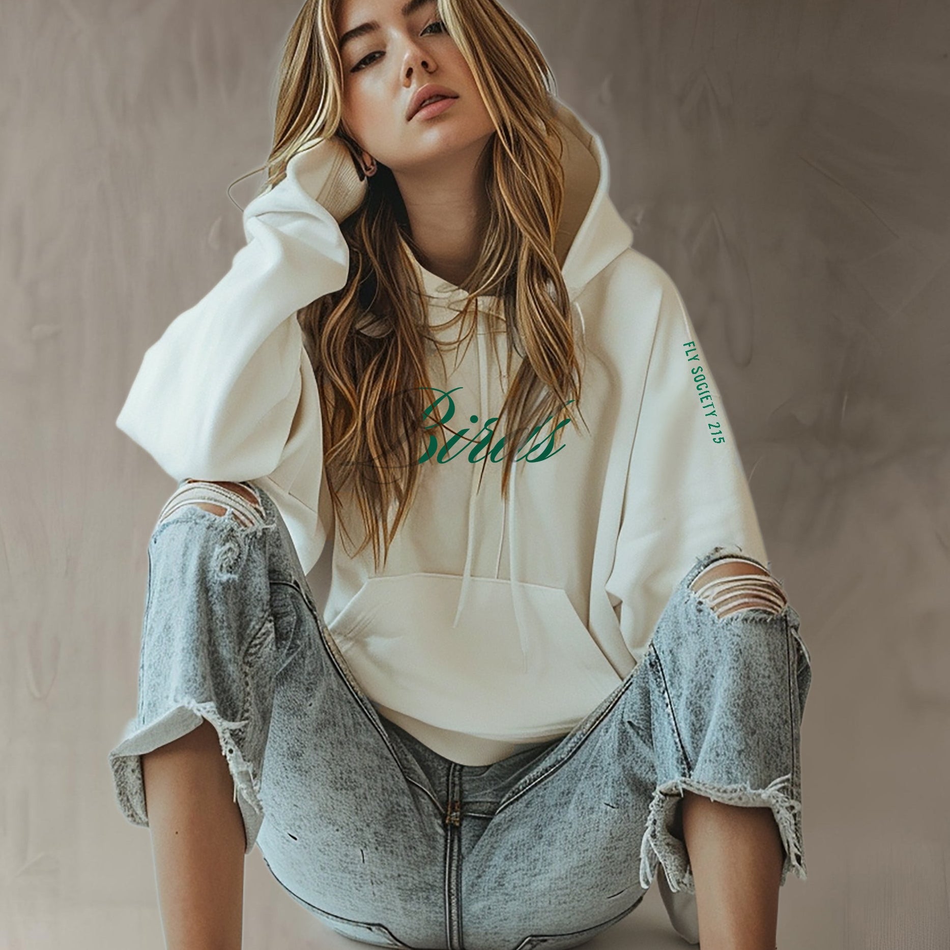 Woman wearing a white hoodie with text and ripped jeans against a neutral background
