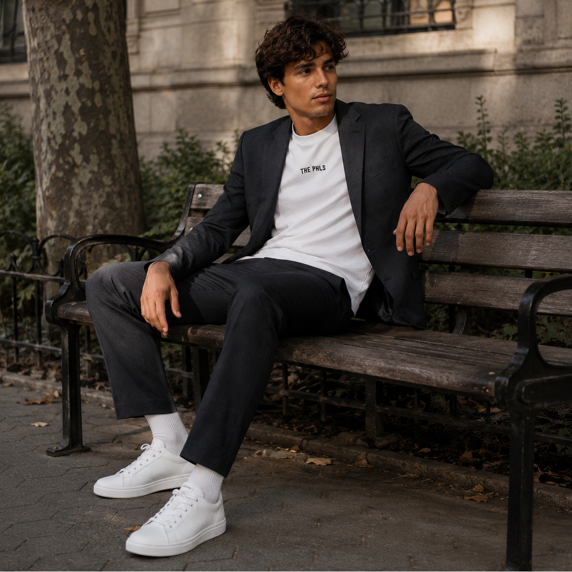 Man sitting on a bench wearing a suit and white sneakers in an urban setting