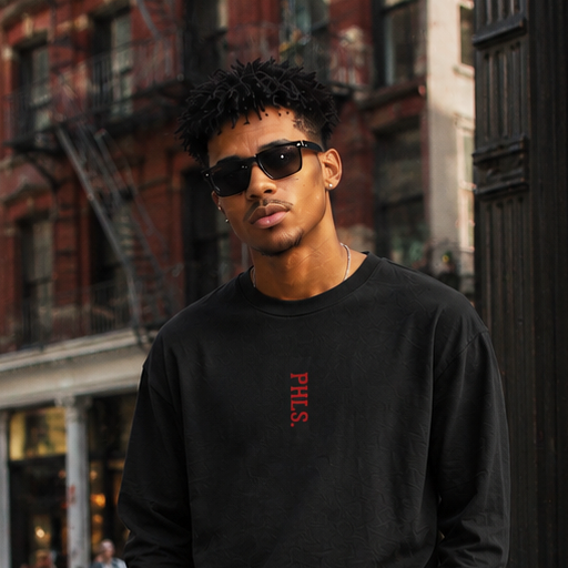 Man wearing a black sweatshirt and cargo pants standing on a city street.