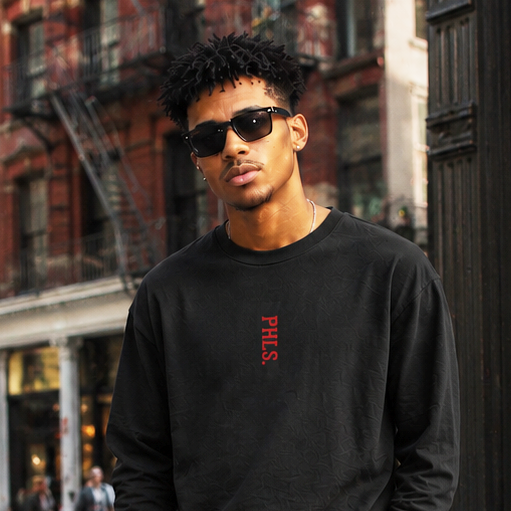 Man wearing a black sweatshirt and cargo pants standing on a city street.