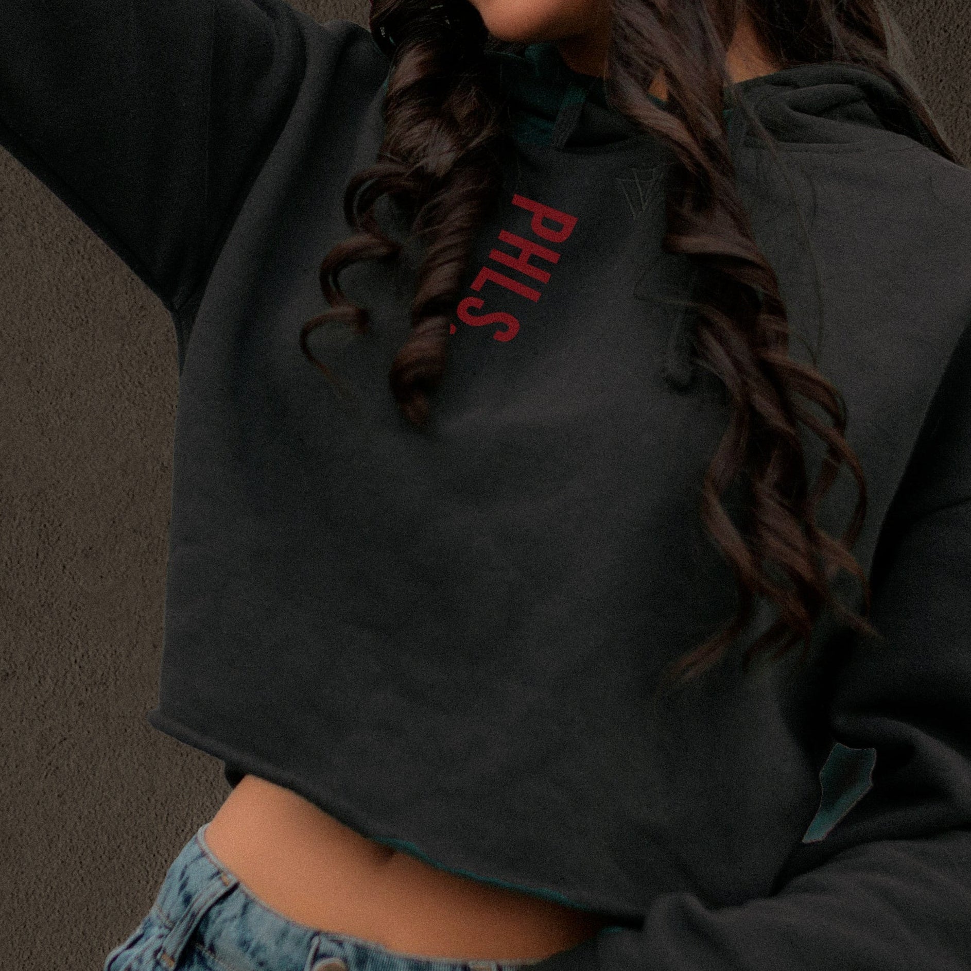Person wearing a black hoodie with red text and blue jeans against a dark background
