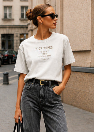 Woman walking on a city street wearing a white t-shirt and gray jeans.