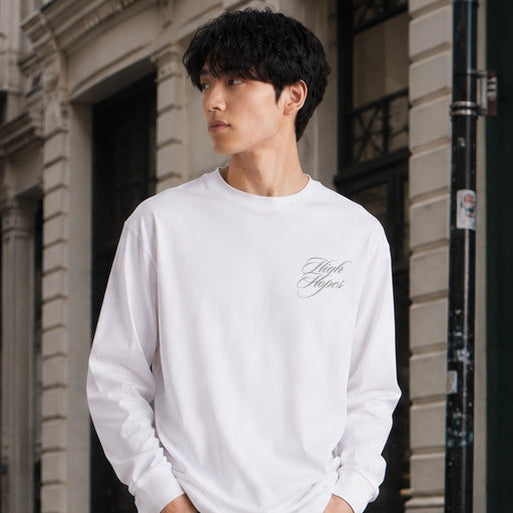 Man wearing a white sweatshirt and dark jeans standing on a city street.