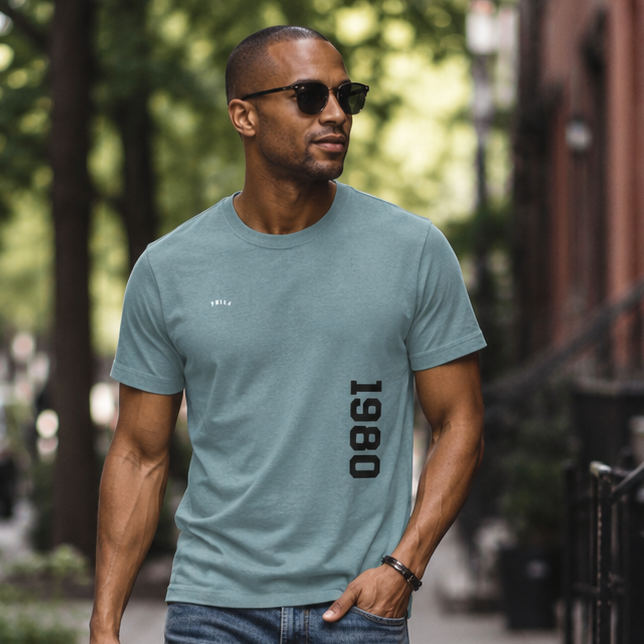 Man walking on a sidewalk wearing a green t-shirt and blue jeans.