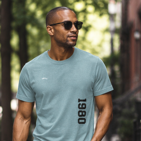 Man walking on a sidewalk wearing a teal t-shirt and blue jeans.
