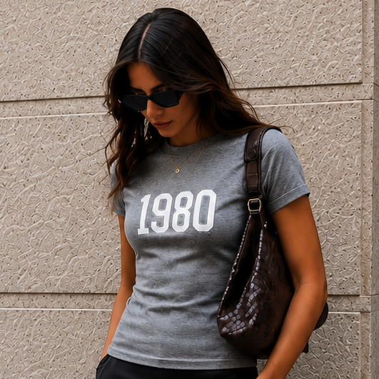 Woman wearing a gray t-shirt with '1980' printed on it, standing against a textured wall.