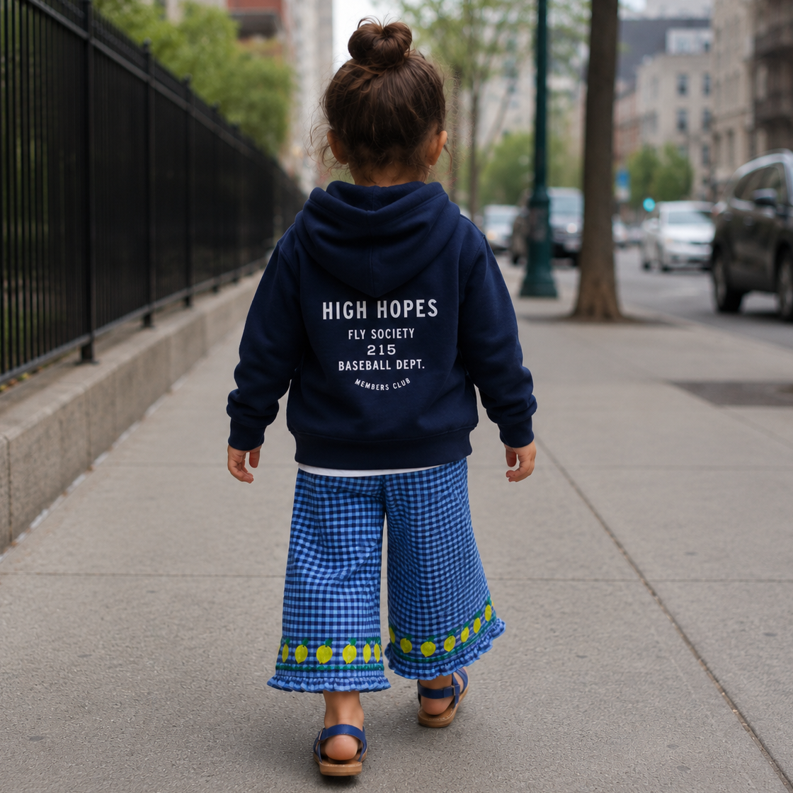 Child wearing a navy hoodie with text, walking on a sidewalk in an urban setting.