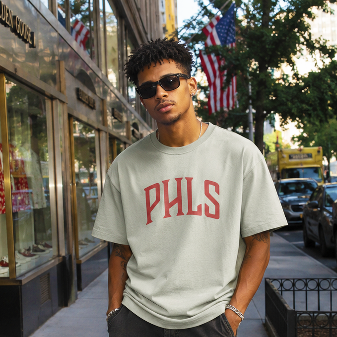 Man wearing a gray 'PHLS' t-shirt on a city street