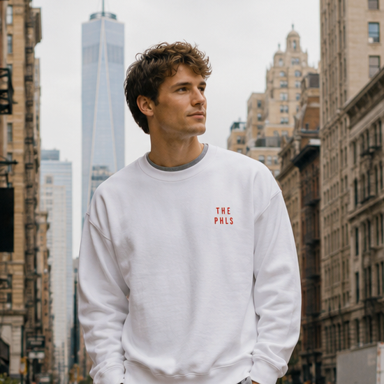 Man wearing a white sweatshirt with a red logo and gray shorts standing on a city street.