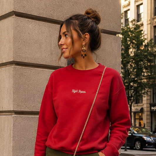 Woman in a red sweatshirt and green shorts standing on a city street.