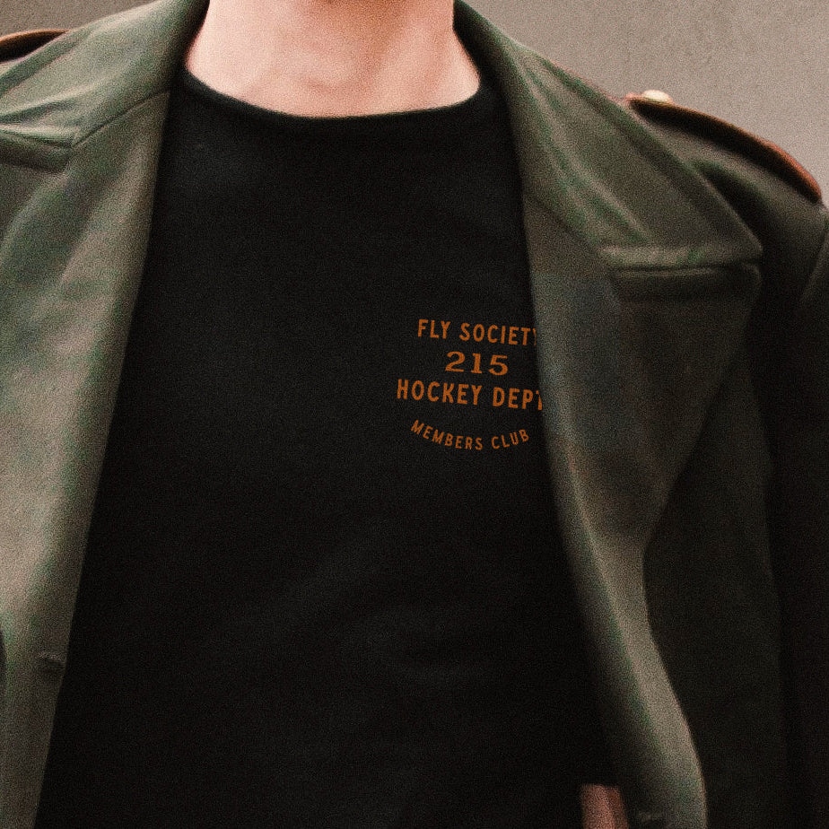 Man wearing a dark green coat over a black t-shirt with text, against a neutral background