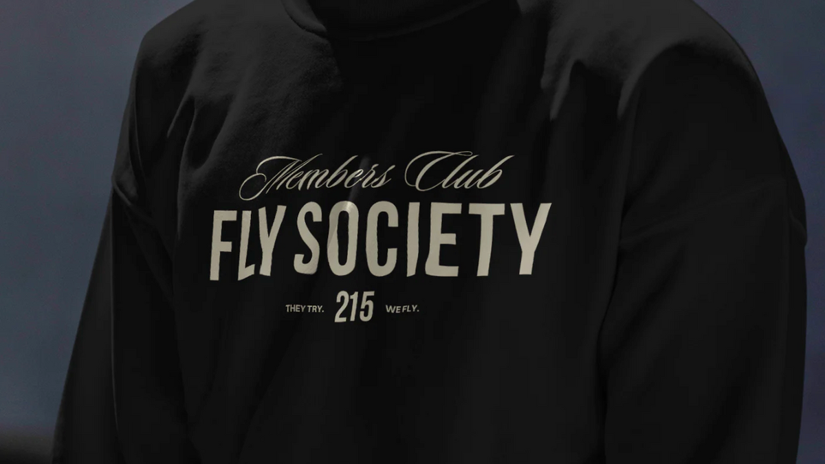 Person wearing a black hoodie with 'Fly Society' text on a dark background