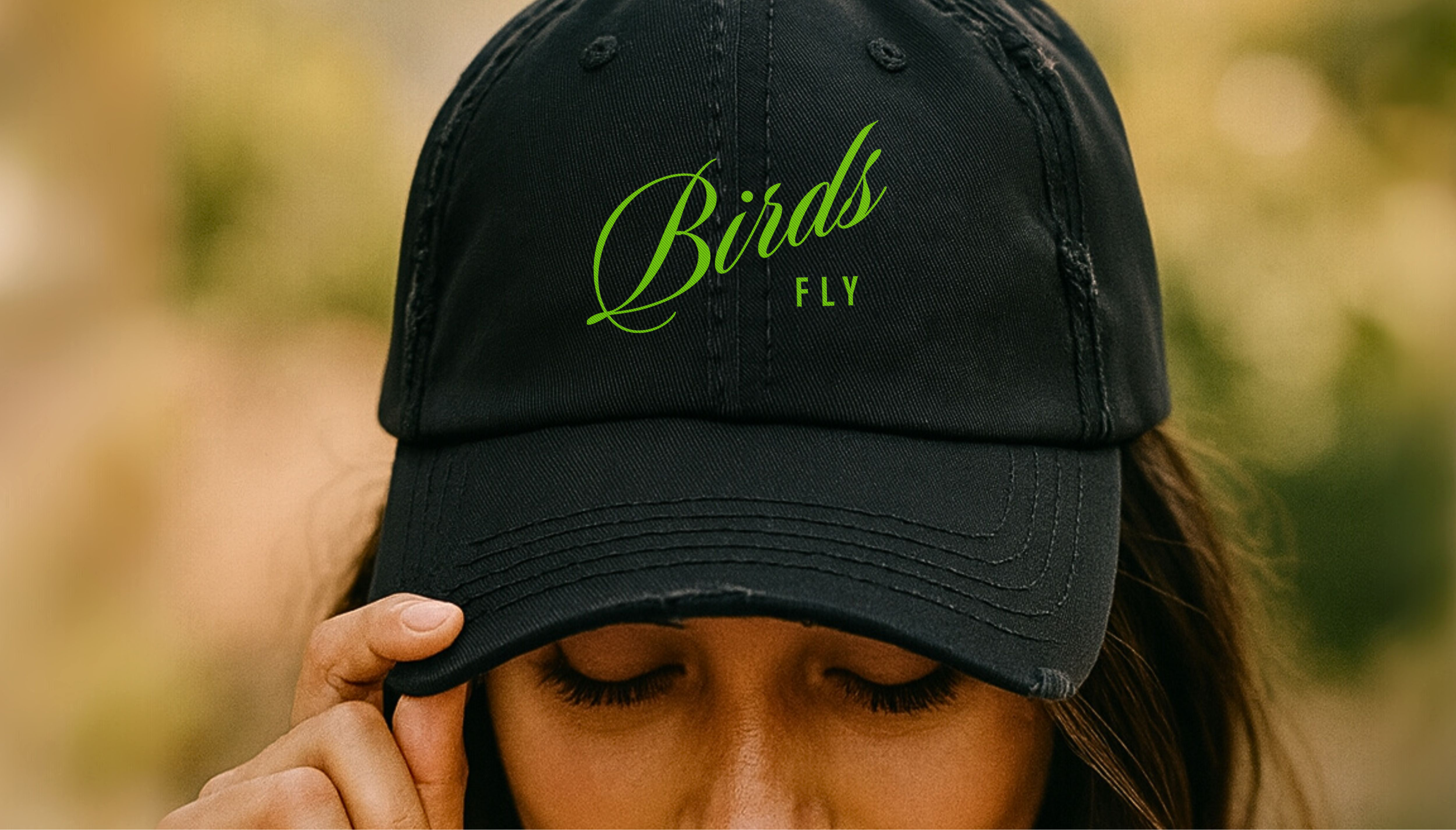 Woman wearing a black cap with 'Birds Fly' text, outdoors.